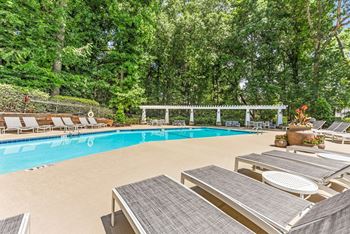 A pool surrounded by trees and lounge chairs. at Southpark Commons Apartment Homes, Charlotte, North Carolina